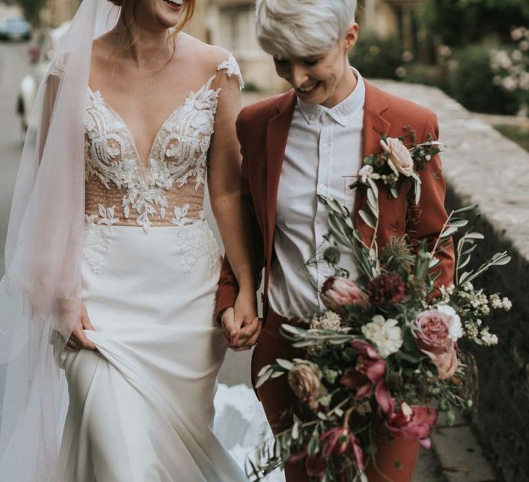 Brides holding hands walking through picturesque Wiltshire village