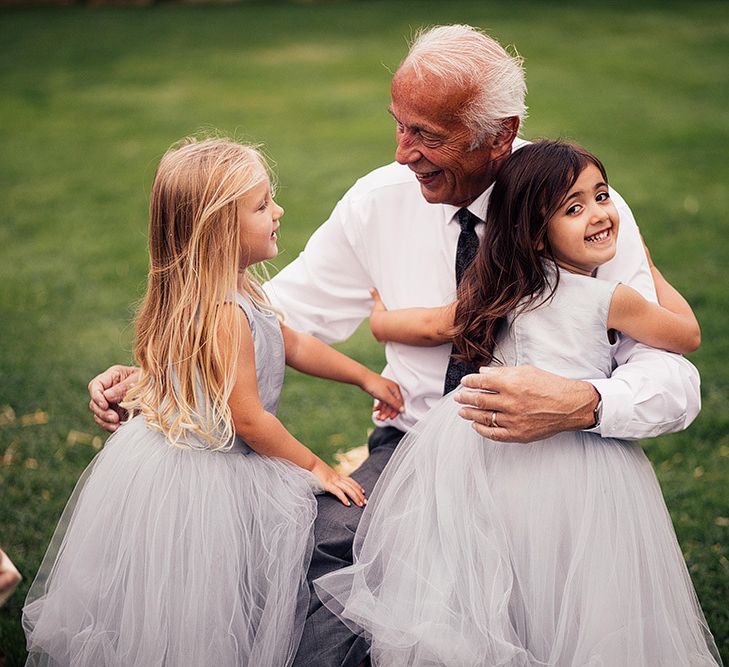 Grandad cuddling the little flower girls in grey tulle dresses