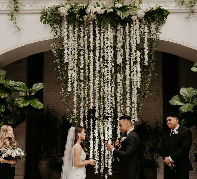 White wedding flowers drape over couple as they say their vows