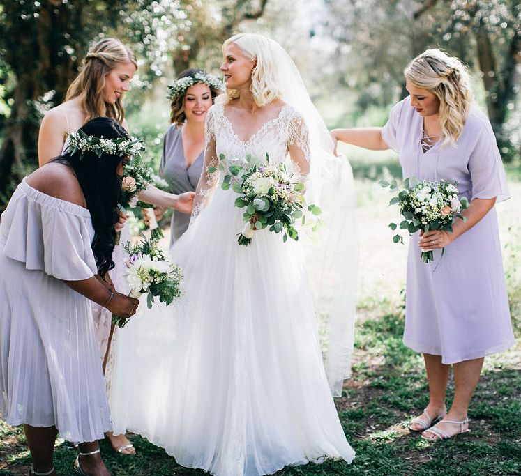 Bride in Long Sleeved Anna Kara Wedding Dress with Lace Bodice and Soft Skirt | Britten Weddings Floor Length Veil | Bridesmaids in Mismatched Lilac Dresses | Bouquets of White, Soft Pink, Purple and Yellow Flowers with Greenery | Flower Crowns | Puglian Countryside Wedding with Fairy Light Altar and Olive Grove Aperitivo | Figtree Wedding Photography