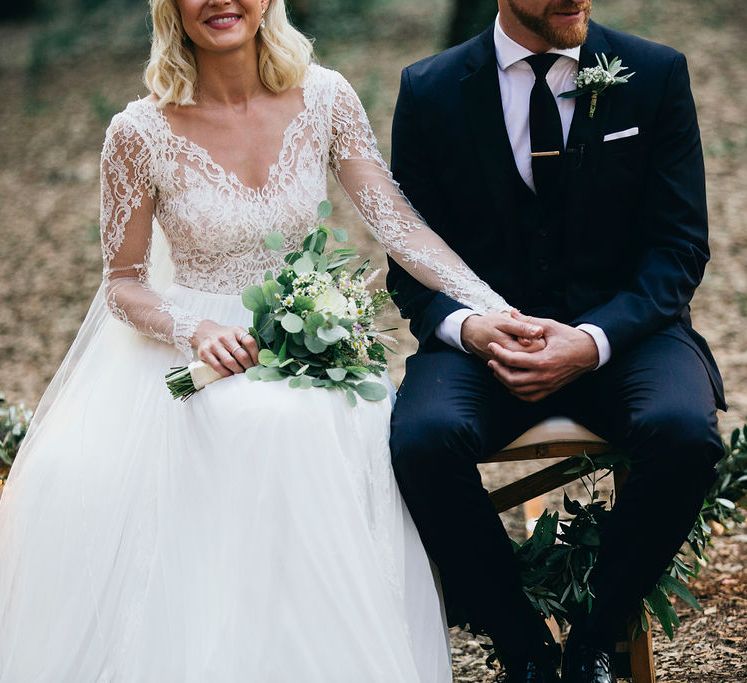 Outdoor Wedding Service | Bride in Long Sleeved Anna Kara Wedding Dress with Lace Bodice and Soft Skirt | Britten Weddings Floor Length Veil | Bridal Bouquet of White, Soft Pink, Purple and Yellow Flowers with Greenery | Groom in Dark Navy Hugo Boss Suit with Waistcoat and Black Patent Shoes by Common Projects | Puglian Countryside Wedding with Fairy Light Altar and Olive Grove Aperitivo | Figtree Wedding Photography