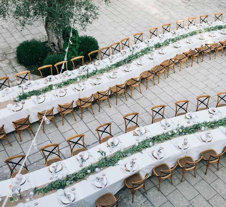 Outdoor Wedding Reception Decor at Tenuta Tresca | Long Tables Snaking Through Courtyard | Foliage Table Runners | Festoon Lights | Knotted Lilac Napkins | Tall Stemmed Candle Holders | Puglian Countryside Wedding with Fairy Light Altar and Olive Grove Aperitivo | Figtree Wedding Photography