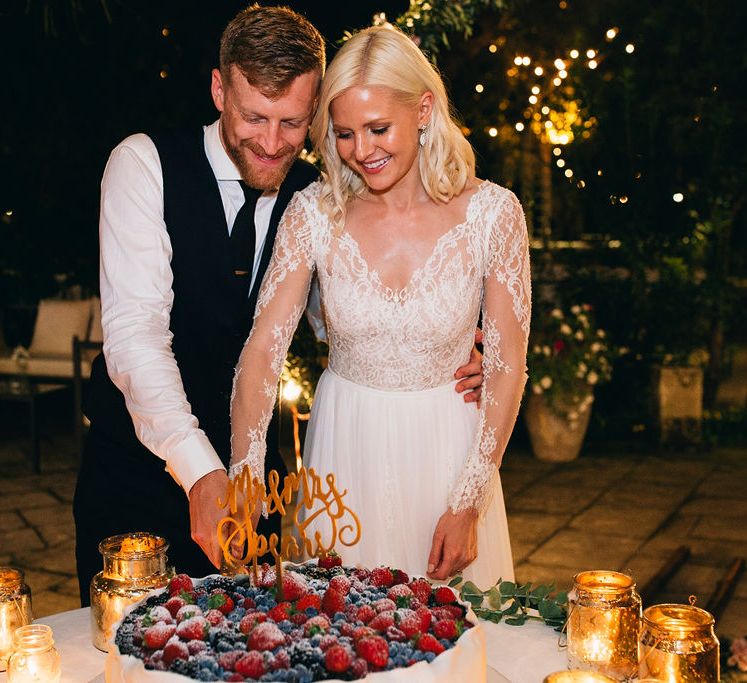 Cutting of the Cake | Traditional Puglian Wedding Cake with Cream, Pastry and Berries | Mr and Mrs Gold Cake Topper | Gold Lanterns | Bride in Long Sleeved Anna Kara Wedding Dress with Lace Bodice and Soft Skirt | Groom in Dark Navy Hugo Boss Suit with Waistcoat and Black Patent Shoes by Common Projects | Puglian Countryside Wedding with Fairy Light Altar and Olive Grove Aperitivo | Figtree Wedding Photography