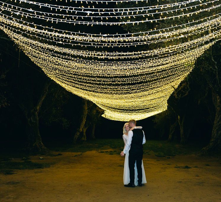 First Dance | Fairylight Canopy | Bride in Long Sleeved Anna Kara Wedding Dress with Lace Bodice and Soft Skirt | Groom in Dark Navy Hugo Boss Suit with Waistcoat and Black Patent Shoes by Common Projects | Puglian Countryside Wedding with Fairy Light Altar and Olive Grove Aperitivo | Figtree Wedding Photography