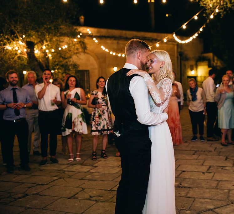 First Dance | Festoon Lights | Glitter Station | Bride in Long Sleeved Anna Kara Wedding Dress with Lace Bodice and Soft Skirt | Groom in Dark Navy Hugo Boss Suit with Waistcoat and Black Patent Shoes by Common Projects | Puglian Countryside Wedding with Fairy Light Altar and Olive Grove Aperitivo | Figtree Wedding Photography