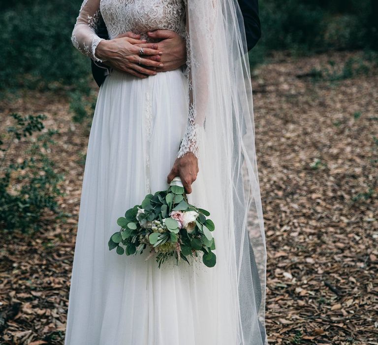 Bride in Long Sleeved Anna Kara Wedding Dress with Lace Bodice and Soft Skirt | Britten Weddings Floor Length Veil | Bridal Bouquet of White, Soft Pink, Purple and Yellow Flowers with Greenery | Groom in Dark Navy Hugo Boss Suit with Waistcoat and Black Patent Shoes by Common Projects | Puglian Countryside Wedding with Fairy Light Altar and Olive Grove Aperitivo | Figtree Wedding Photography