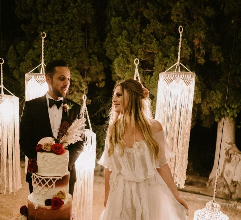 Bride and Groom Cutting the Wedding Cake in Front of Macrame Chandeliers