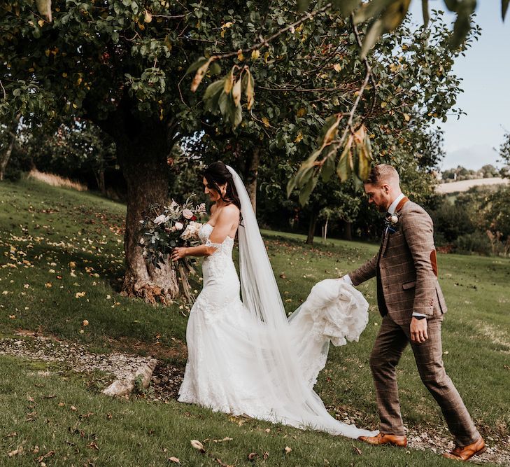 Groom in brown checked suit holding his brides wedding dress train