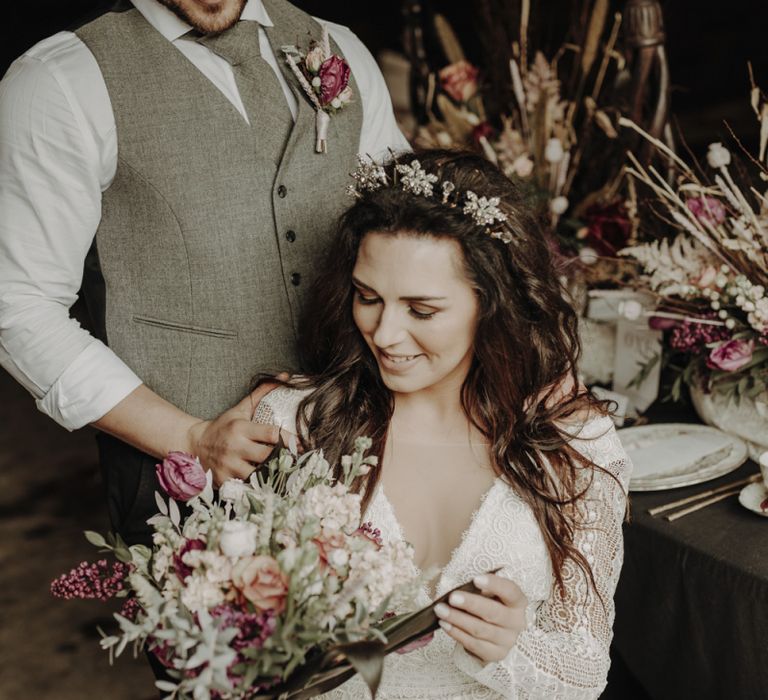 Boho Bride in Lace Wedding Dress Looking at White and Purple Wedding Bouquet