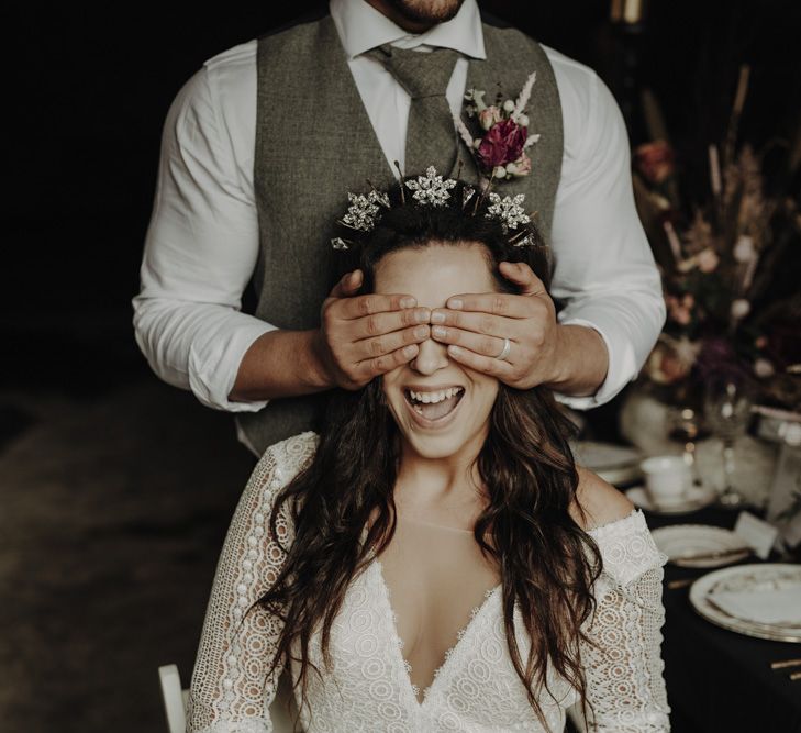 Groom in Wool Waistcoat covering Brides Eyes  in Lace Wedding Dress and Crown Headpiece