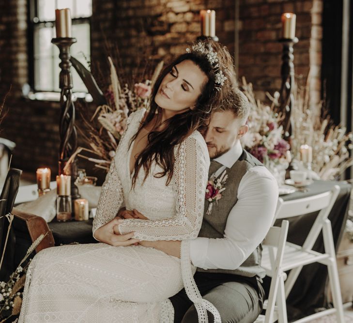 Boho Bride in Lace Wedding Dress and Groom in Wool Waistcoat Sitting at Rustic Tablescape with Dried Flower Decor and Floral Tableware