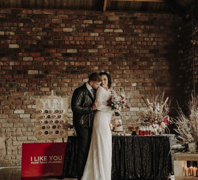 Boho Bride in Lace Wedding Dress and Groom in Leather Jacket Standing at Dessert Table