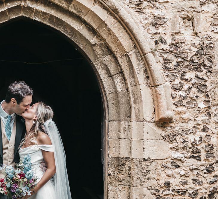 Groom in morning suit kisses his bride at church wedding door