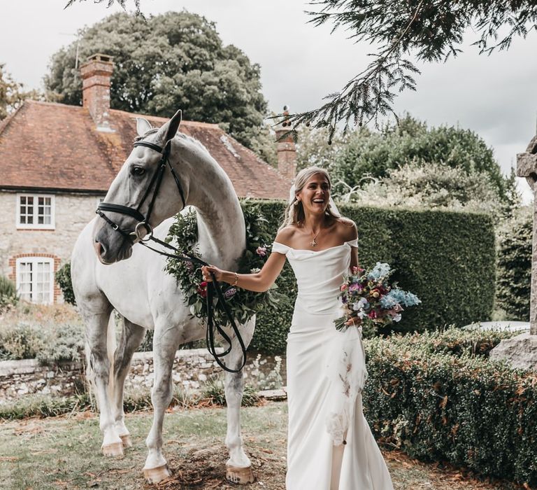 Bride in Bardot wedding dress and her pet horse with flower collar