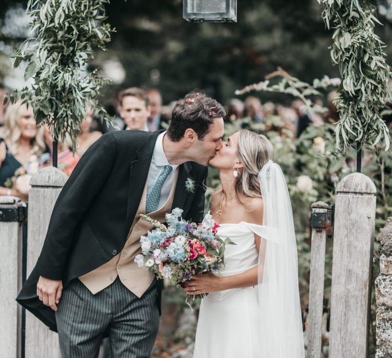 Bride and groom kissing at local church gates