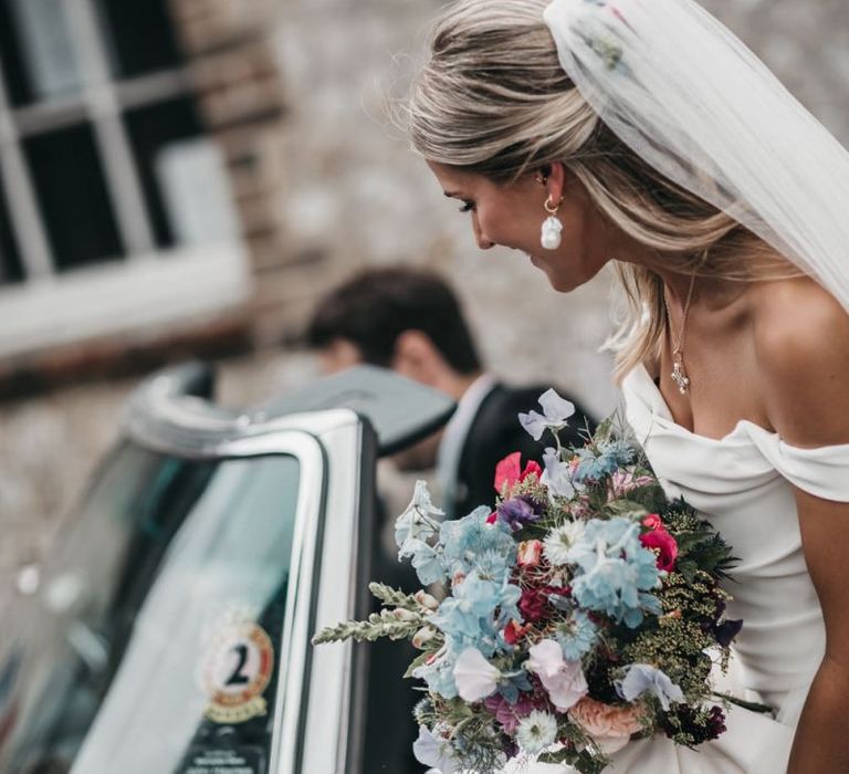 Bride holding a blue and pink wild flower bouquet  gets into the wedding car