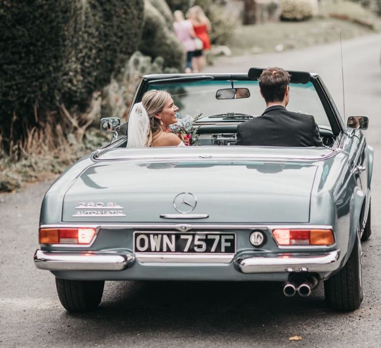 Bride and groom drive off in a blue convertible wedding car