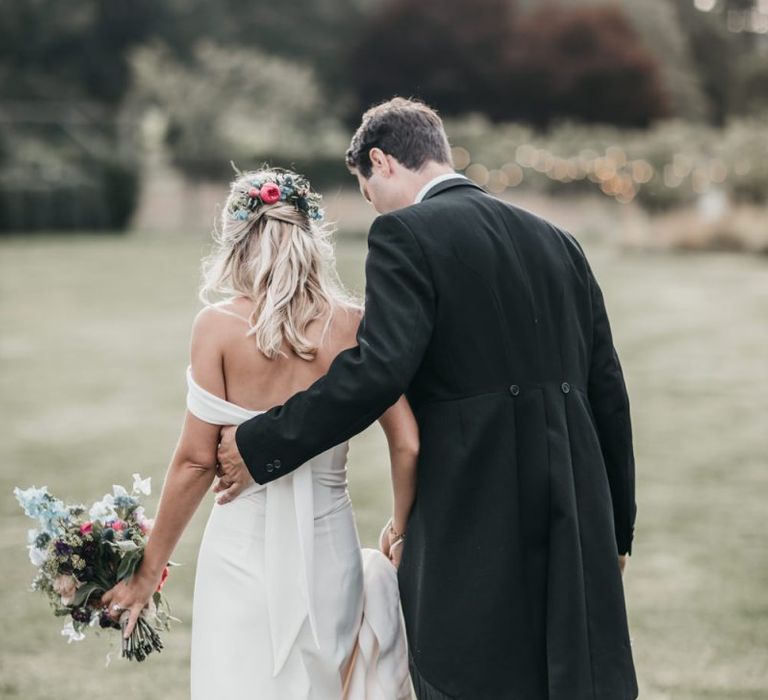 Groom in tails with his arm around his bride in a Bardot wedding dress