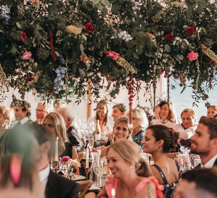 Wedding guests sitting under a wildflower installation