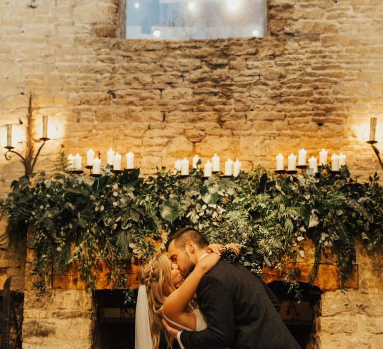 Bride and groom kissing in from of the fireplace at Cripps Barn