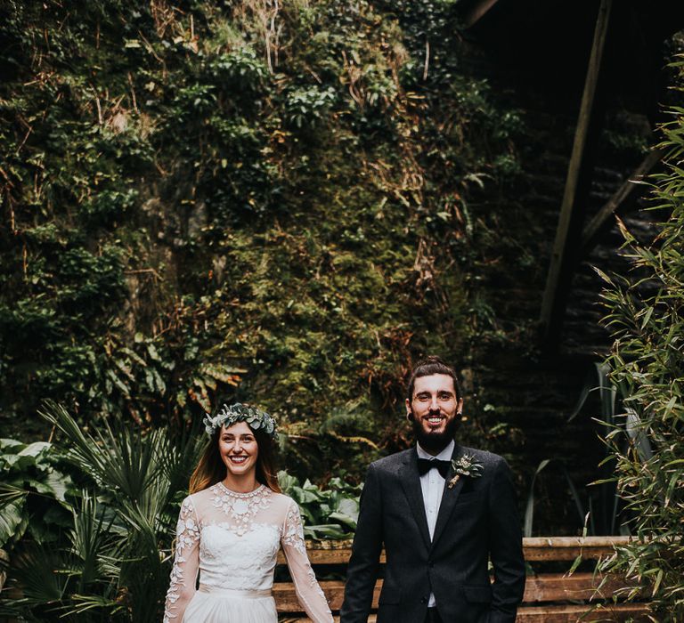 Stylish Bride in Catherine Deane Separates and Flower Crown and Groom in Tuxedo  Holding Hands