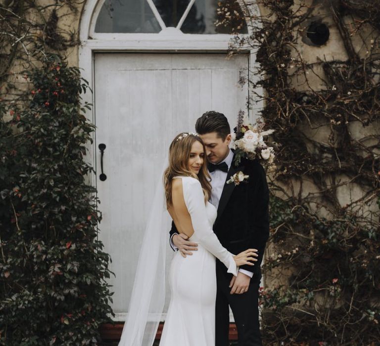 Bride in Backless Emma Beaumont Wedding Dress and Groom in Tuxedo Embracing