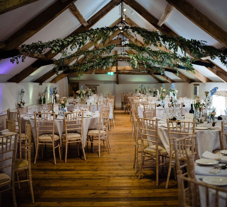 Pennard House Wedding Reception Decor with Beams Covered in Foliage and Pastel Wedding Flower Stems in Bottles as Centrepieces