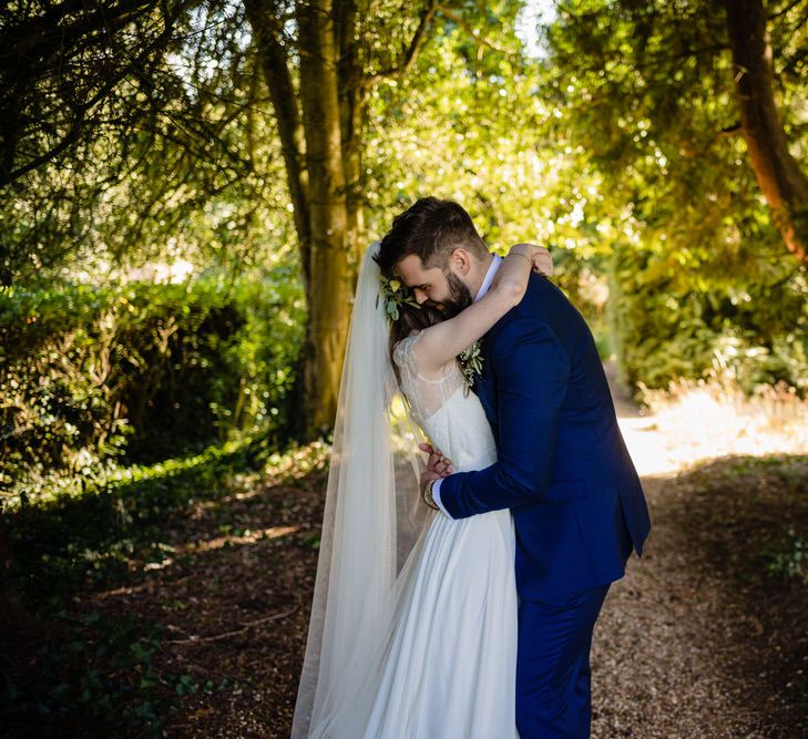 Bride in Charlie Brear Wedding Dress and Olive Flower Crown with Groom in Ted Baker Navy Suit Embracing