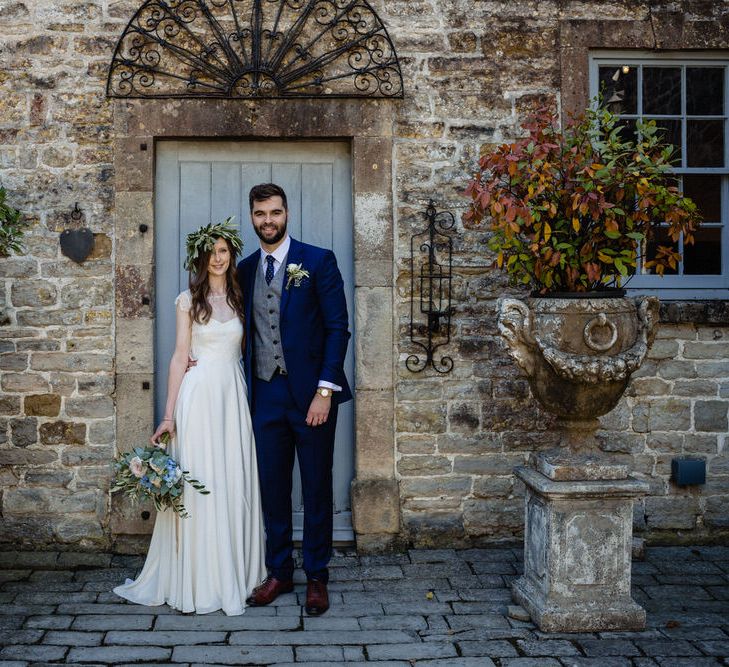 Bride in Charlie Brear Wedding Dress and Olive Flower Crown with Groom in Ted Baker Navy Suit Arm in Arm