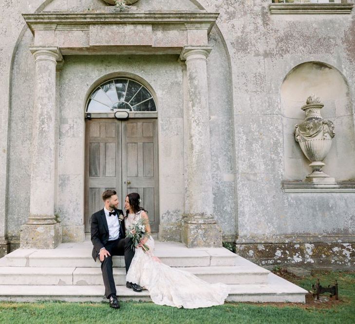 Bride and groom sit on the steps at Lulworth Castle