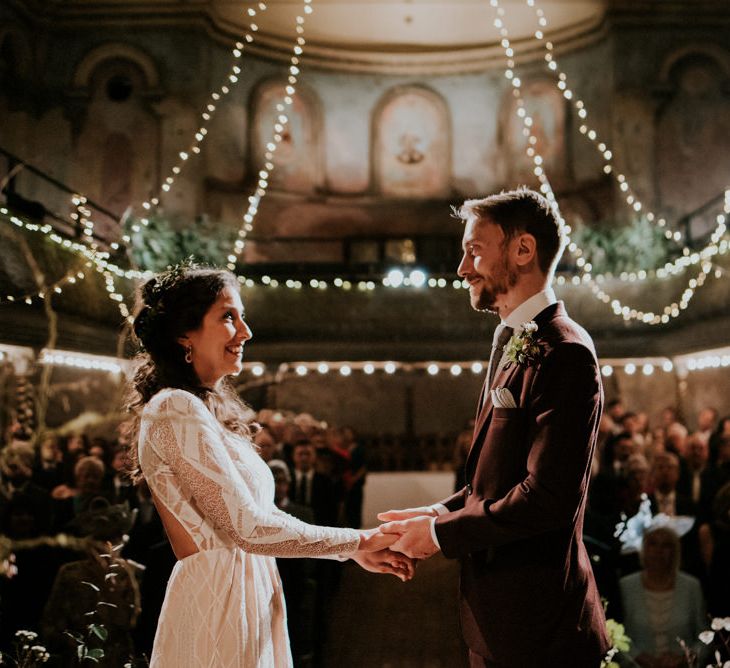 Bride in Grace Loves Lace Wedding Dress and Groom in  Brown Wedding Suit Holding Hands, Exchanging Vows at their Wilton's Hall Wedding Ceremony