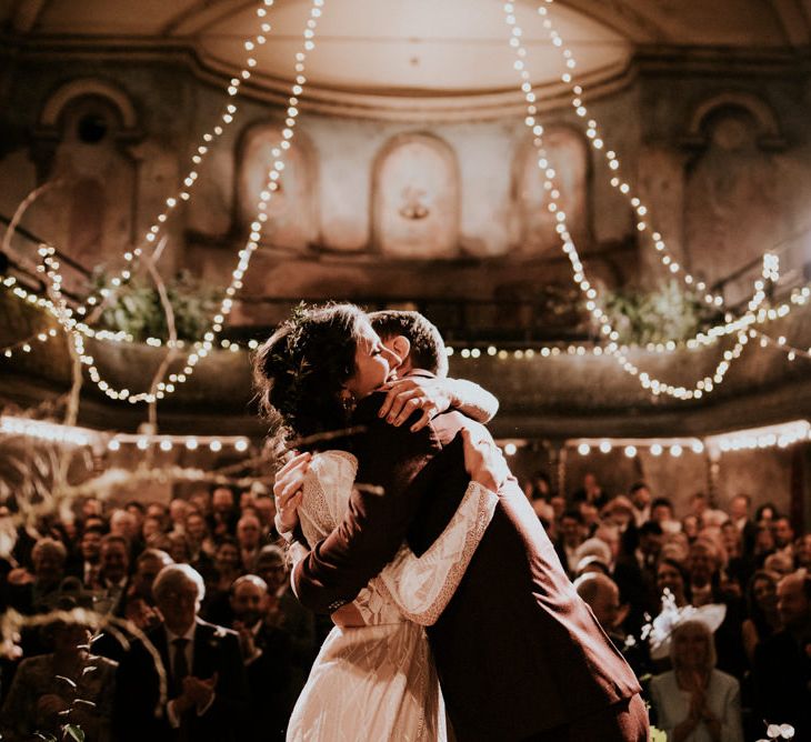 Bride in Grace Loves Lace Wedding Dress and Groom in  Brown Wedding Suit Hugging their Wilton's Hall Wedding Ceremony