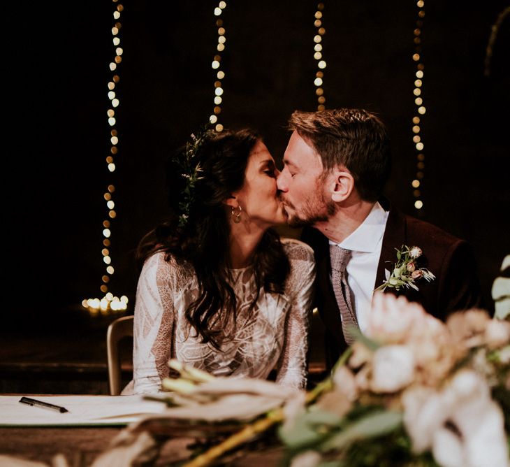 Bride in Grace Loves Lace Wedding Dress and Groom in  Brown Wedding Suit Kissing Whilst Signing The Register