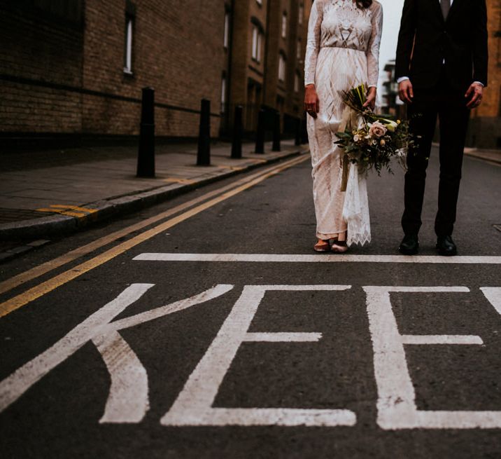 Urban Portrait of Bride in Grace Loves Lace Wedding Dress and Groom in Dark Suit Next to Keep Road Sign