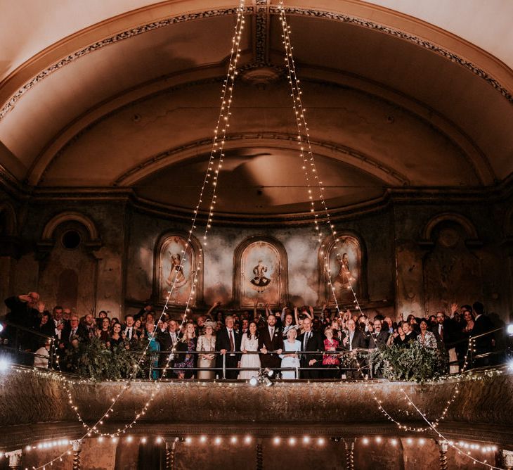 Wedding Guests Posing on top of the Mezzanine at Wilton's Music Hall with Hanging Fairy Lights Decor