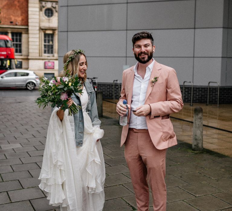 Stylish bride in wedding dress and denim jacket and groom in pink suit