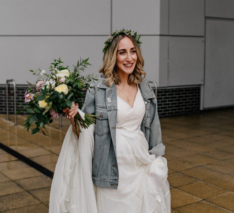 Bride in Catherine Deane wedding dress and denim jacket with flower crown and wedding bouquet