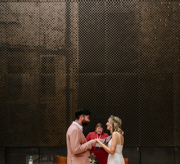 Bride in Catherine Deane wedding dress and groom in pink suit exchanging vows at hackney Town Hall micro wedding