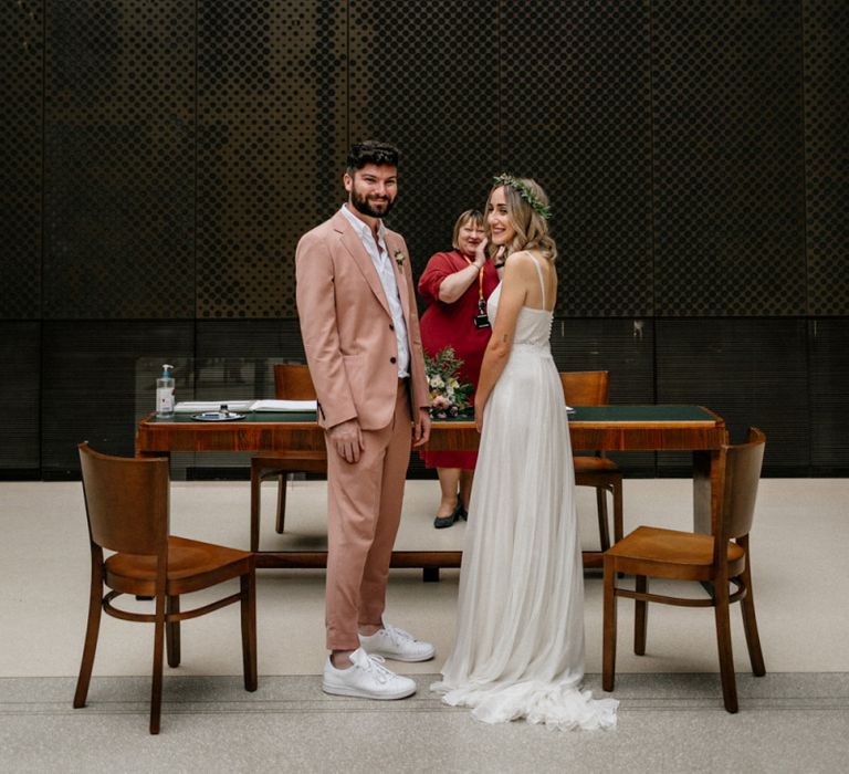 Groom in pink suit and boho bride in floaty dress and flower crown at intimate wedding ceremony