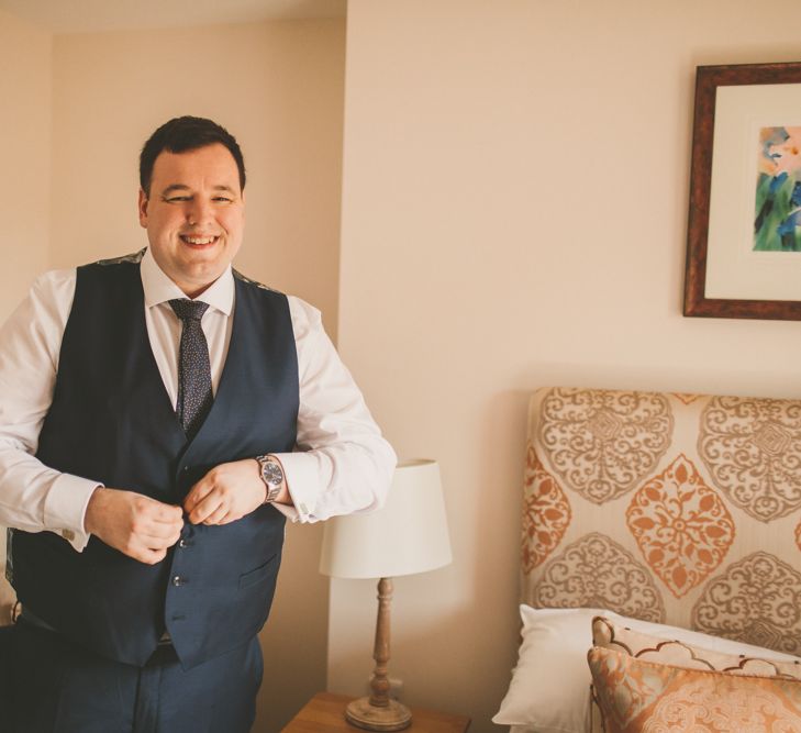 Groom preparations in navy waistcoat for wedding at Bassmead Manor Barns wedding