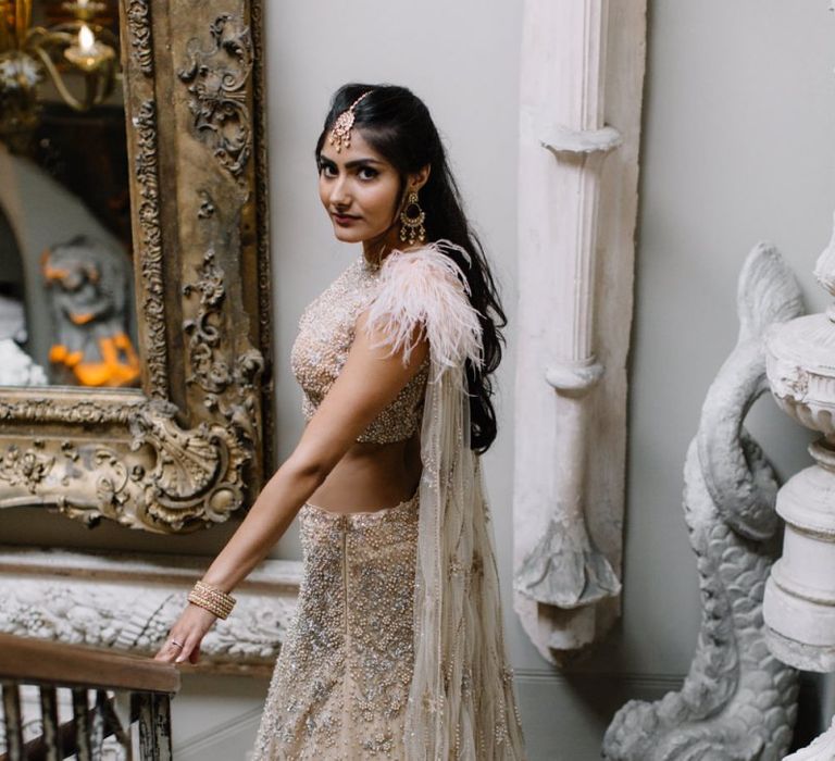 Bride in gold and blush Indian separates with feathers and cape