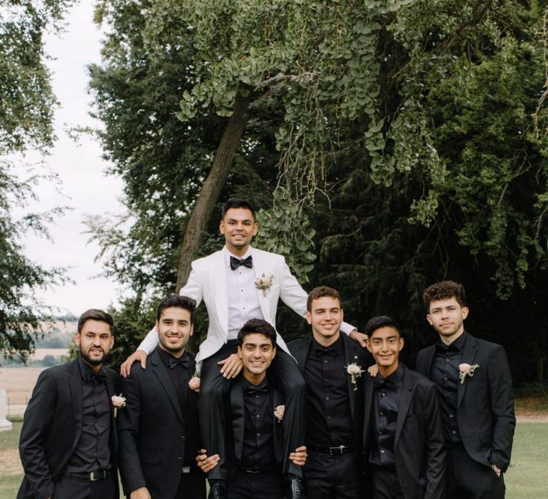 Groomsmen in black shirts and suits and groom in white dinner jacket