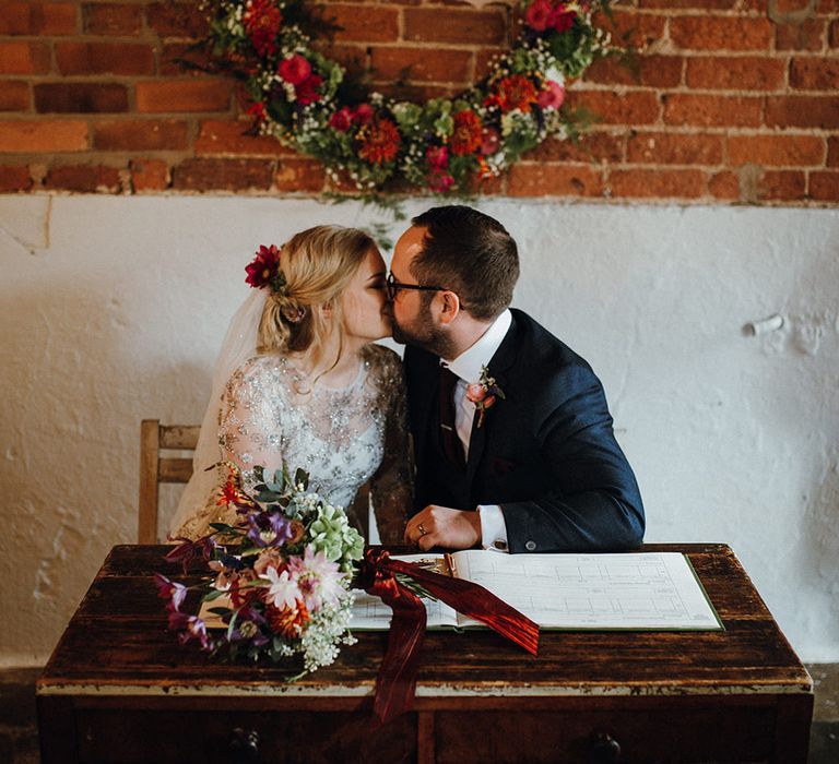 Bride in Bead Embellished Needle &amp; Thread Gown with Cascading Tulle Skirt and Semi-Sheer Sleeves | Elbow Length Veil | Bridal Up Do with Pink Hair Flowers | Groom in Check Blue Three-Piece Suit by T.M.Lewin with Maroon Tie and Pocket Square | Purple, Orange and Pink Flowers with Foliage and Maroon Trailing Ribbon | Floral Wreath Altar | Rustic Bureau | Signing of the Register | Mariachi Band and Persian Rug Aisle for Autumn Wedding | Leah Lombardi Weddings