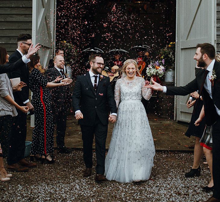 Bride in Bead Embellished Needle &amp; Thread Gown with Cascading Tulle Skirt and Semi-Sheer Sleeves | Elbow Length Veil | Bridal Up Do with Pink Hair Flowers | Groom in Check Blue Three-Piece Suit by T.M.Lewin with Maroon Tie and Pocket Square | Purple, Orange and Pink Flowers with Foliage and Maroon Trailing Ribbon | Confetti Moment | Mariachi Band and Persian Rug Aisle for Autumn Wedding | Leah Lombardi Weddings