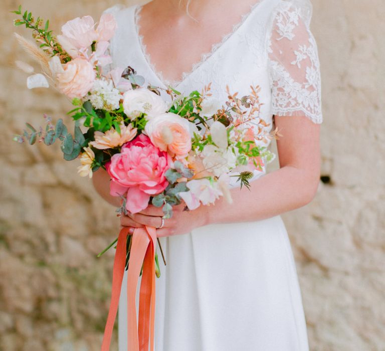 Bride in Lace Cap Sleeve Wedding Dress From Croque Lune Holding Coral , Pink and Peach Wedding Bouquet tied with Ribbons