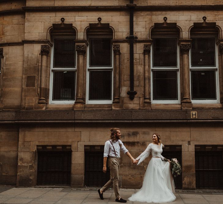 Bride in Separates and Groom in Chinos and Braces Holding Hands Walking Through Manchester Streets