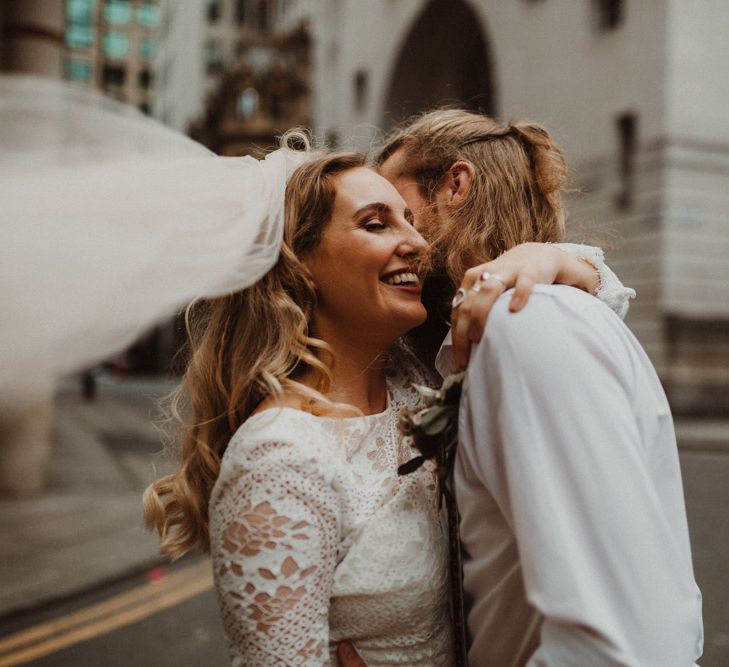 Bride in Separates and Groom in Chinos and Braces Embracing in Manchester Streets