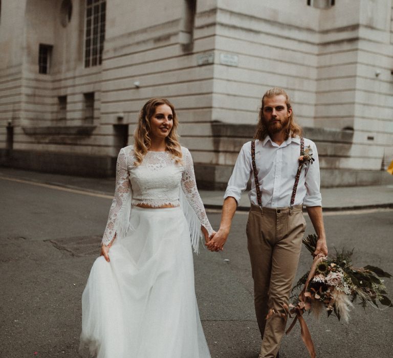 Bride in Separates and Groom in Chinos and Braces Holding Hands Walking Through Manchester Streets