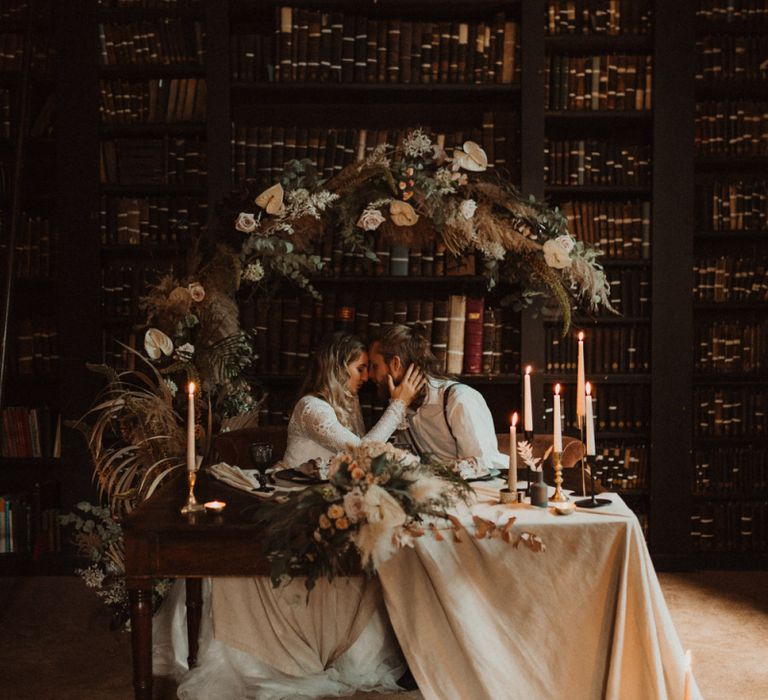 Boho Couple Sitting at Sweetheart Table Decorated with Linen Tablecloth and Taper Candles