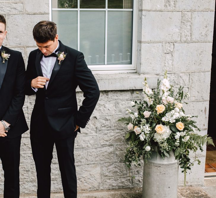 Groom wearing black tie at Wales wedding venue with peach flower displays